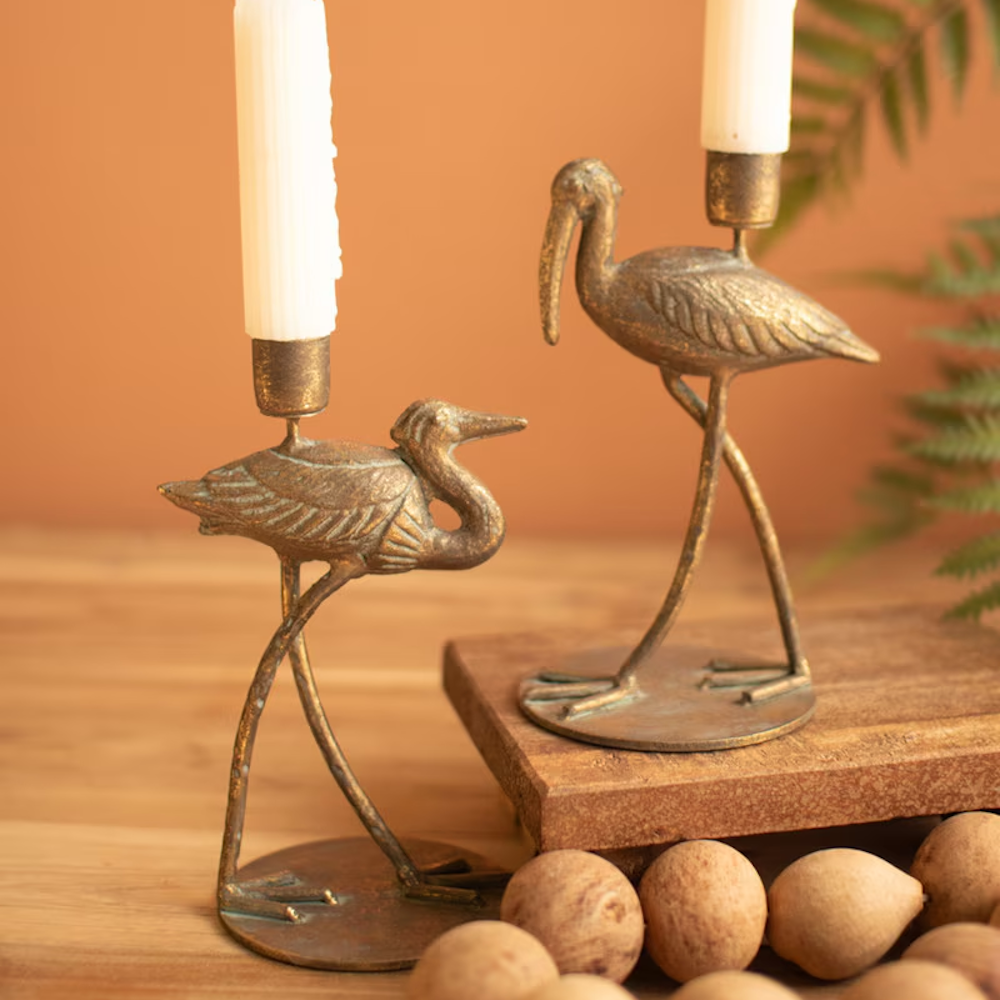 Pair of antique brass shorebird taper candleholders displayed with lit candles on a wooden table.