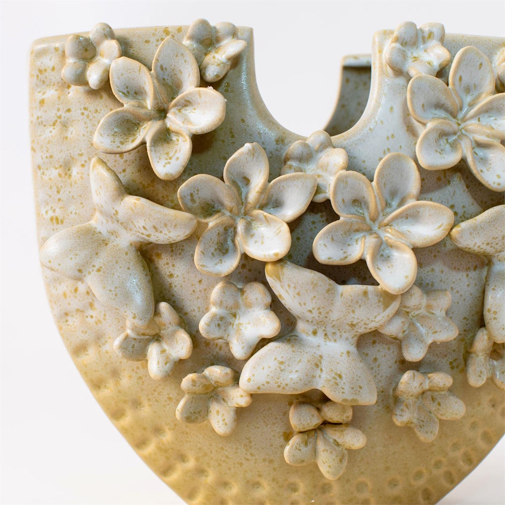 Close-up of a speckled cream ceramic vase featuring 3D embossed butterfly and floral accents in a rustic, textured finish.