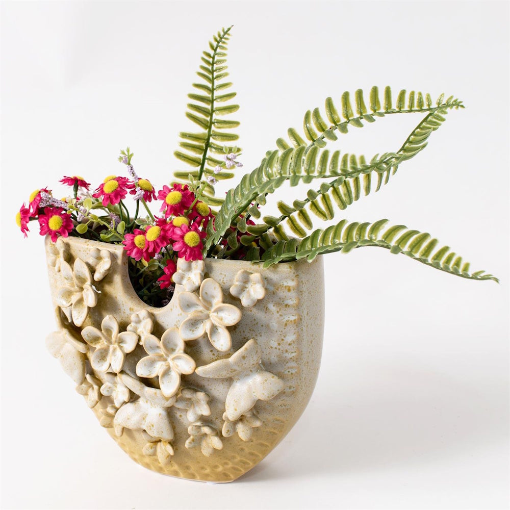 Ceramic butterfly and flower relief vase with pink daisies and green ferns against a white background.
