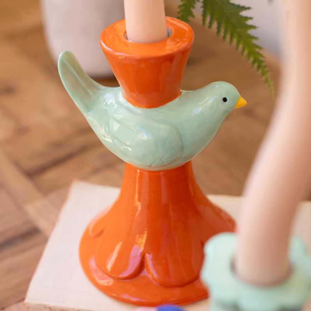Ceramic bird taper candle holder in orange and mint green on a wooden table.