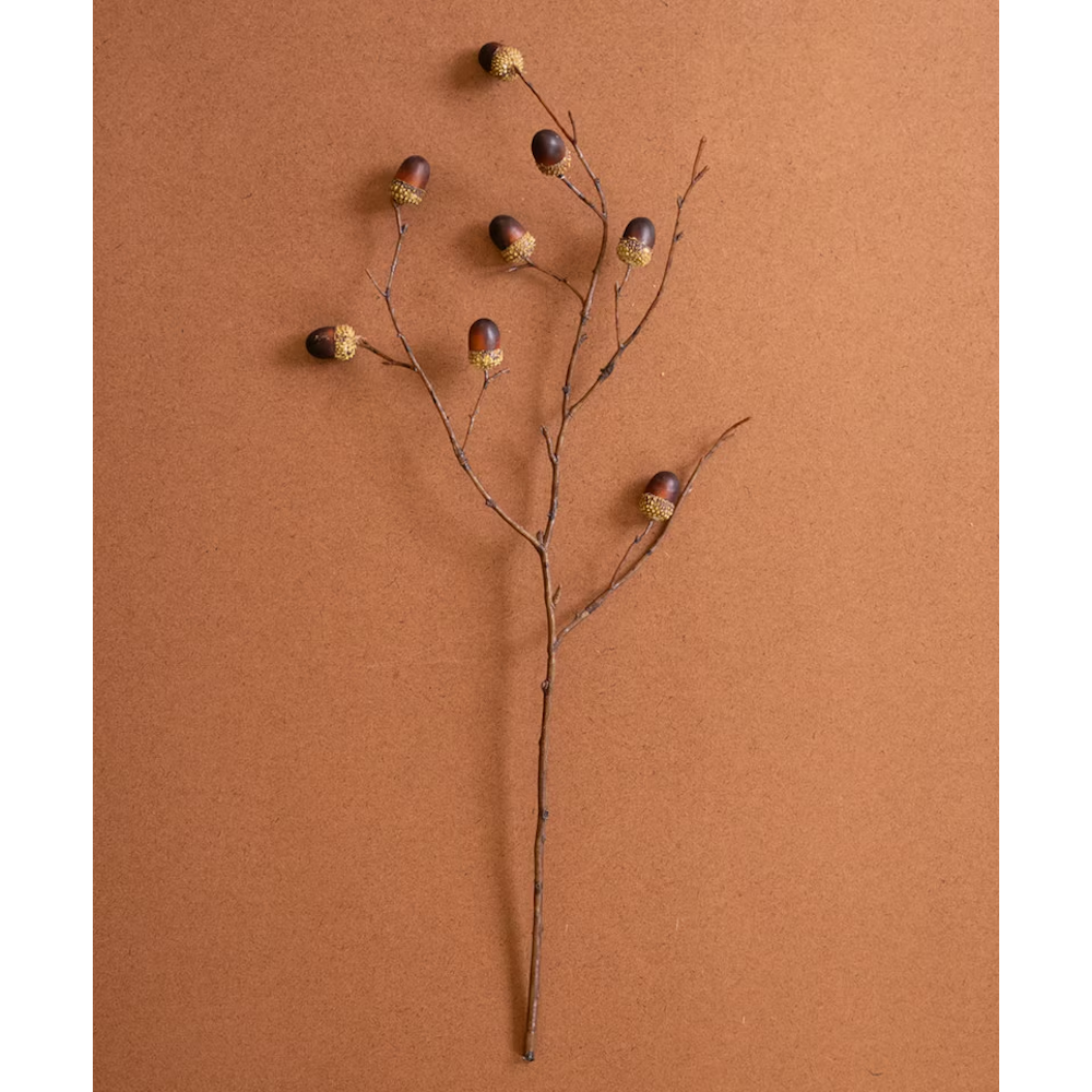 Artificial oak branch stem with small brown acorns lying flat on a warm terracotta surface.