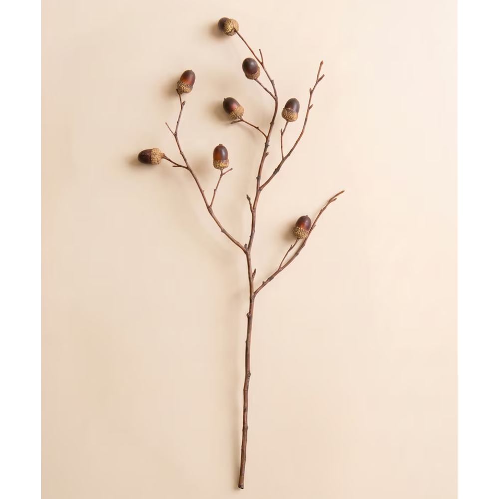Artificial oak branch stem with small brown acorns displayed flat against a beige background.