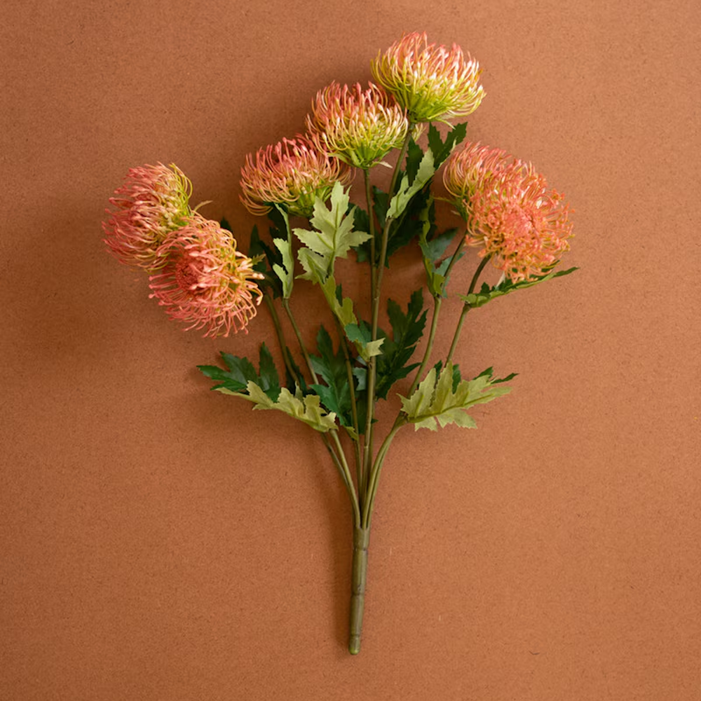 Artificial antique blush pincushion protea spray displayed flat on a warm terracotta background.