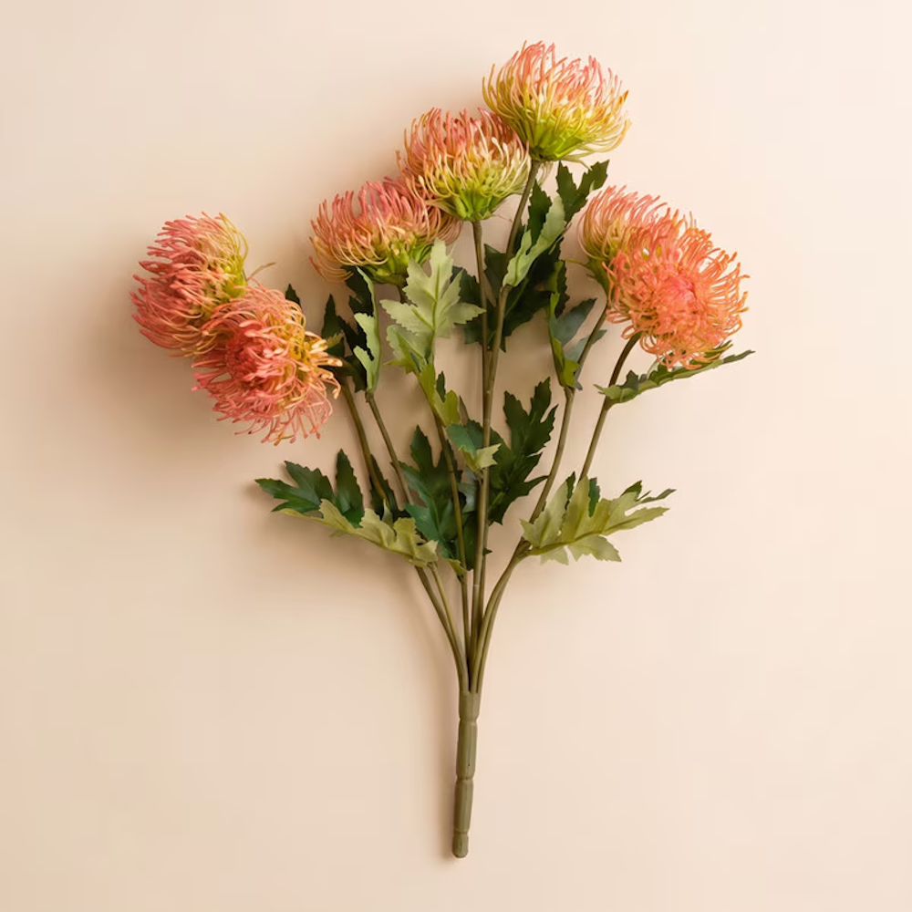 Artificial antique blush pincushion protea spray with green leaves on a light cream background.