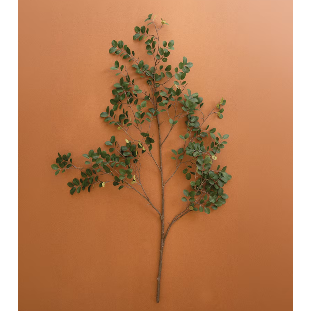Single artificial green crape myrtle branch stem lying flat against a warm terracotta background.