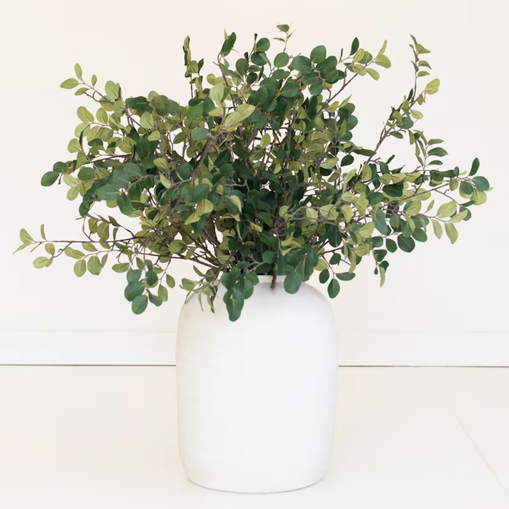 Full arrangement of leafy green artificial crape myrtle spray stems styled in a white ceramic vase.