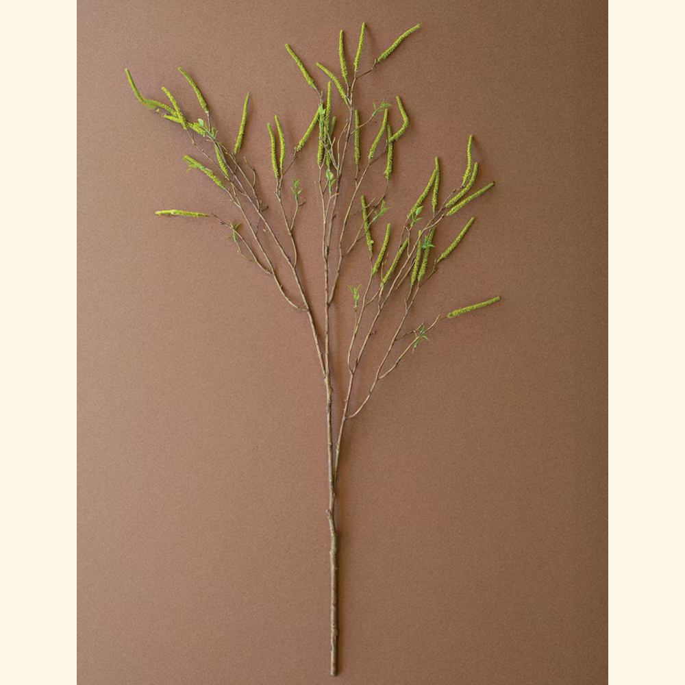 Artificial green willow flower spray with budding catkins on a slender brown branch against a brown background.