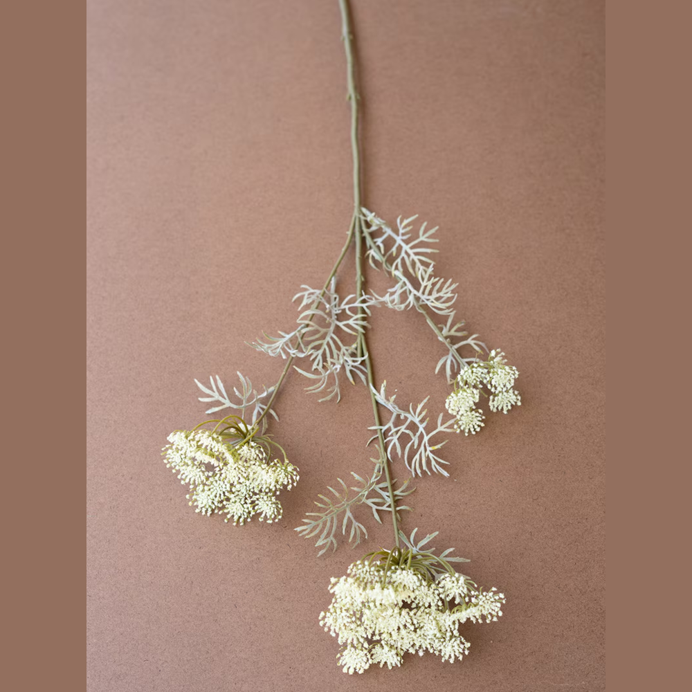 Artificial white lace flower spray with delicate green leaves on a brown background.