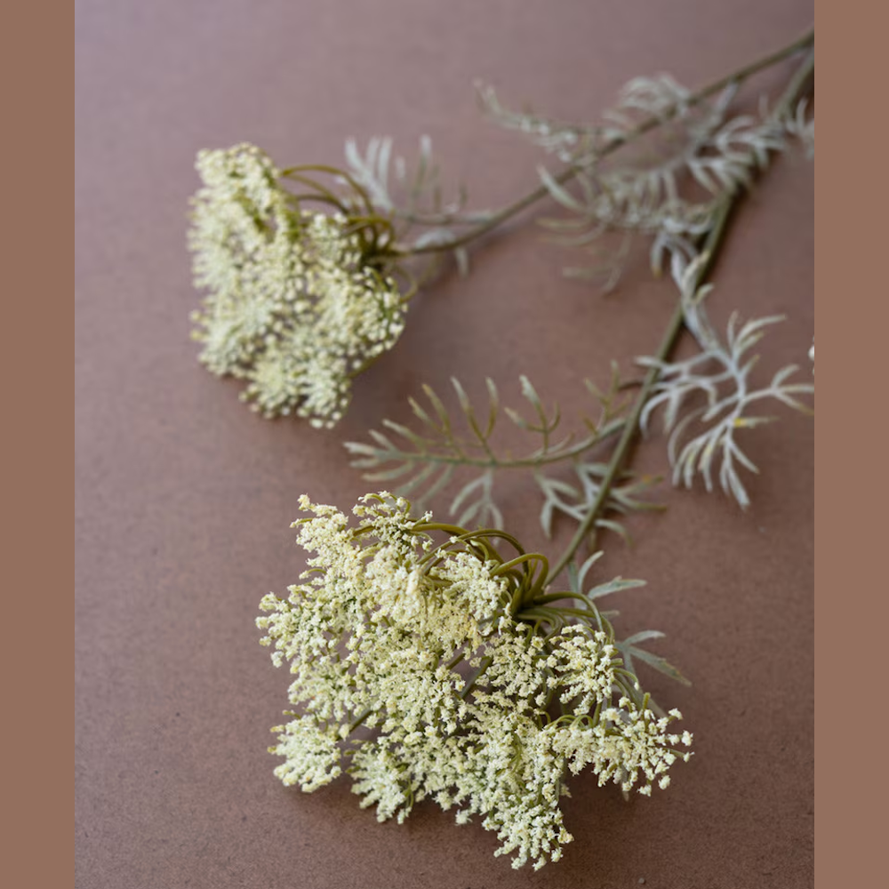 Artificial cream Queen Anne's lace flower spray with green leaves on a brown background for home decor and floral arrangements.
