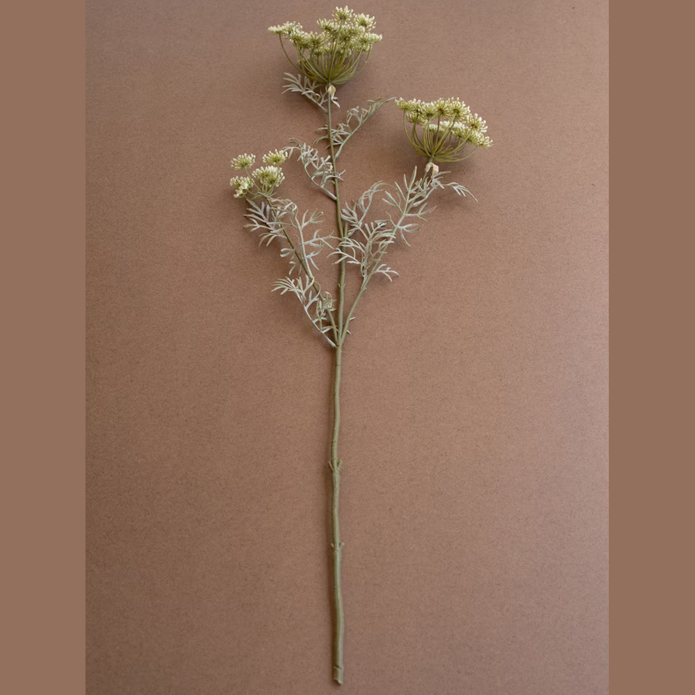 Artificial cream lace flower spray with green leaves and stem on a brown background.