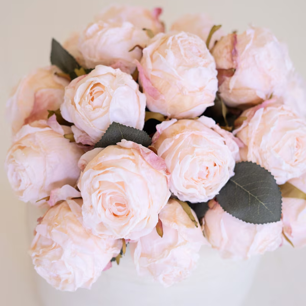 Close-up view of soft blush pink artificial rose blooms clustered together with green leaves.