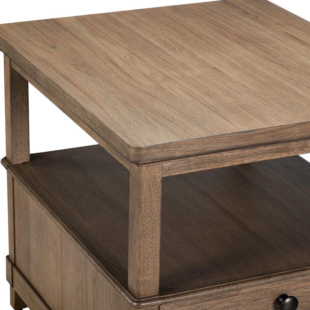 Close-up corner view of a warm brown wood end table with a smooth tabletop, open shelf, and drawer.