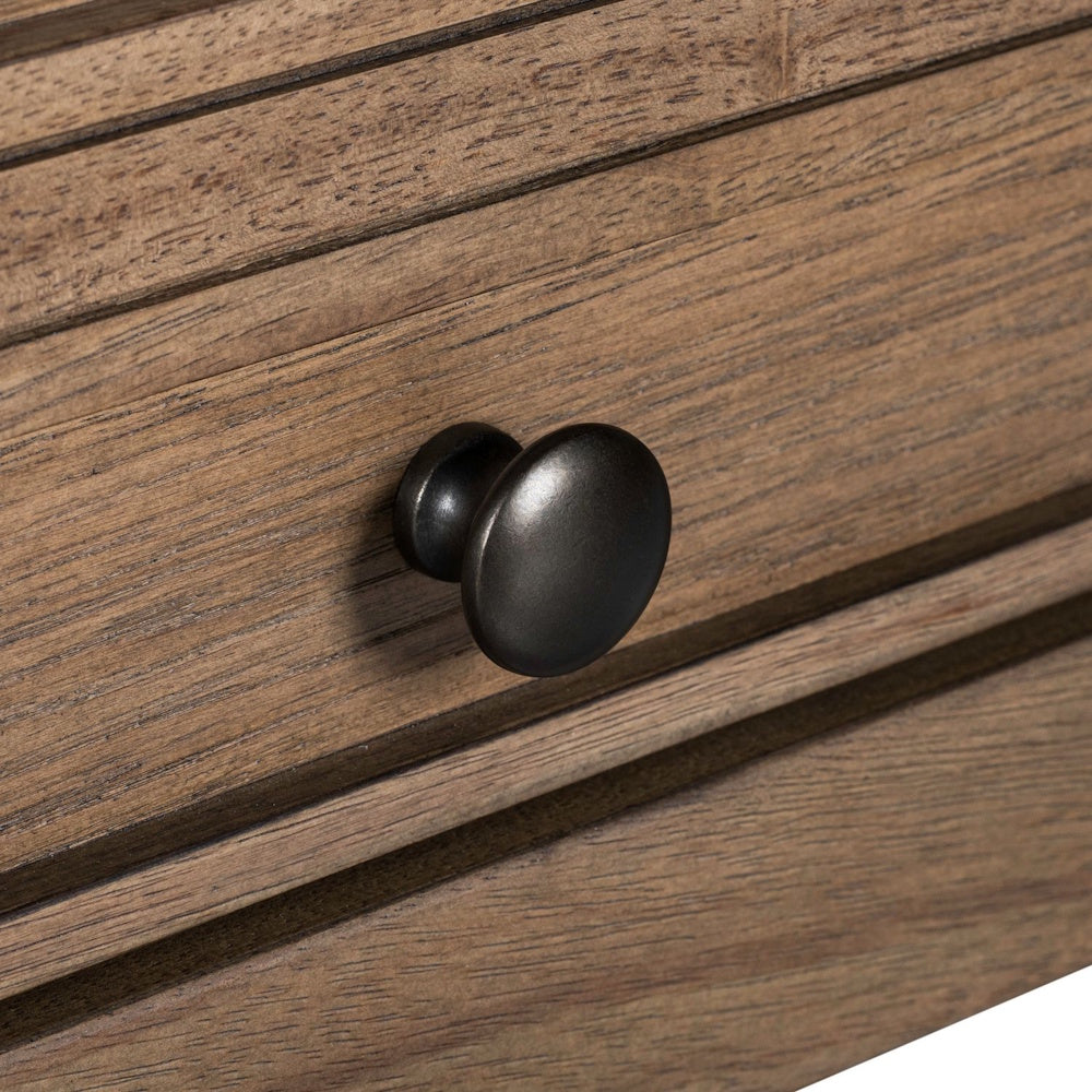 Close-up of a dark bronze metal round knob on a natural wood drawer front.