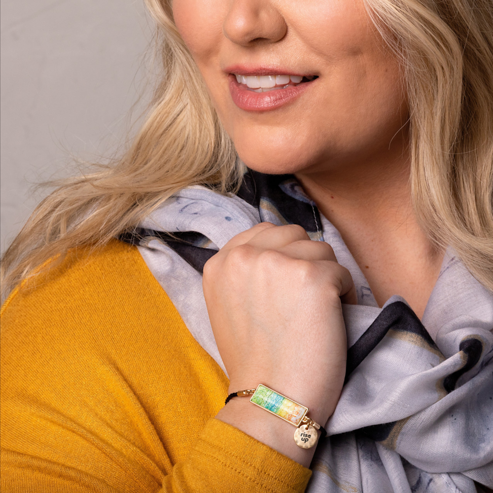 Close-up of a woman wearing a yellow top and a multi-colored rectangular charm bracelet that says "rise up".