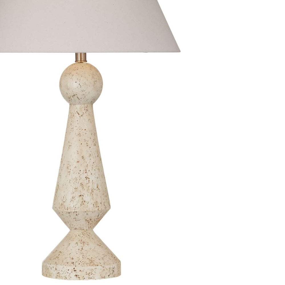Close-up of a speckled beige table lamp base with a geometric sculpted silhouette beneath a cream shade.