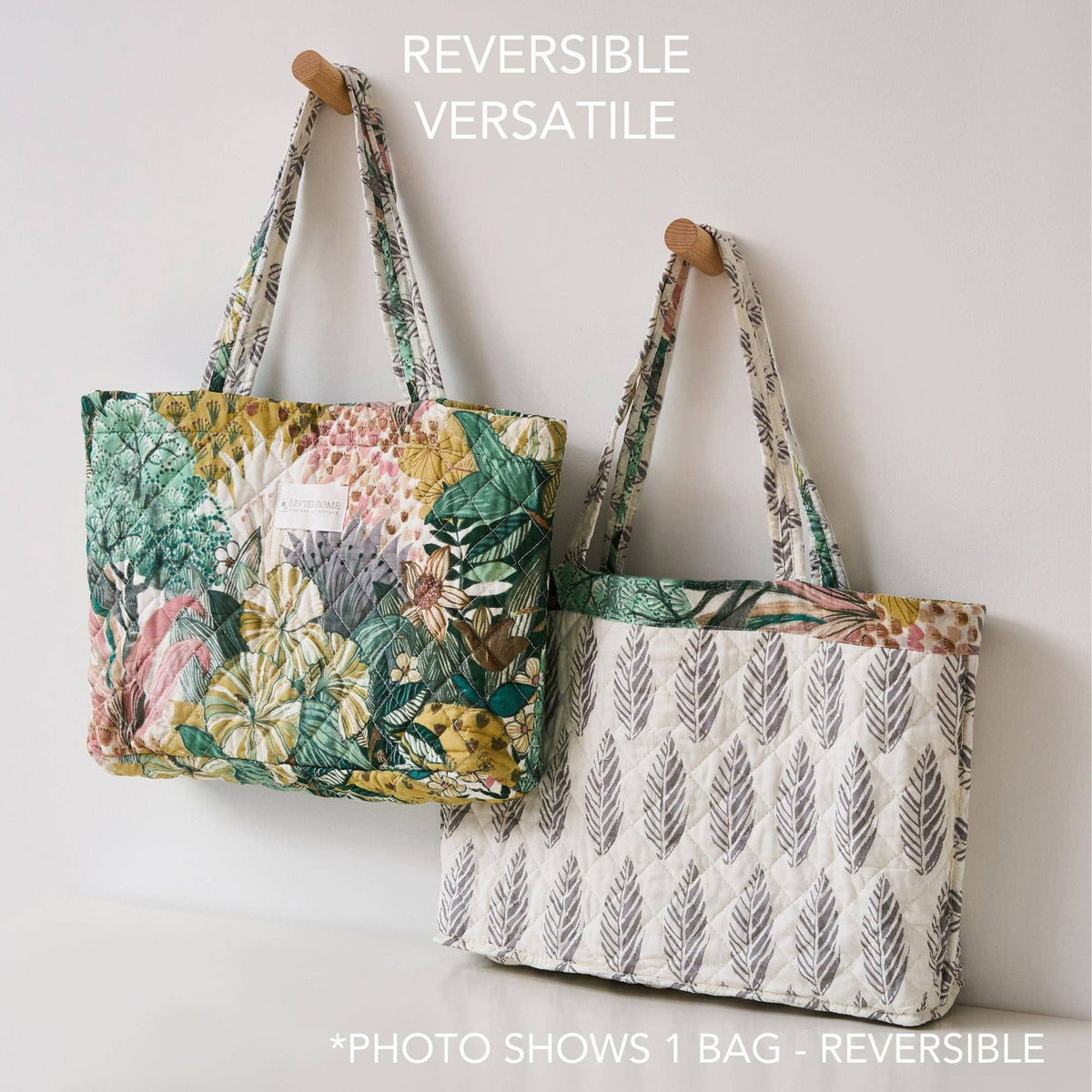 Reversible quilted tote bag with floral and leaf patterns hanging on wooden pegs, versatile cotton handbag.