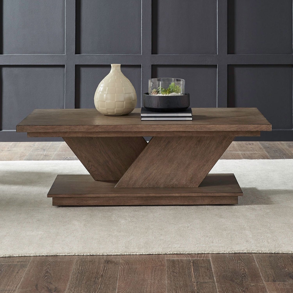Aspen Sky cocktail table with decorative vase and planter on a beige rug against a dark grey paneled wall.
