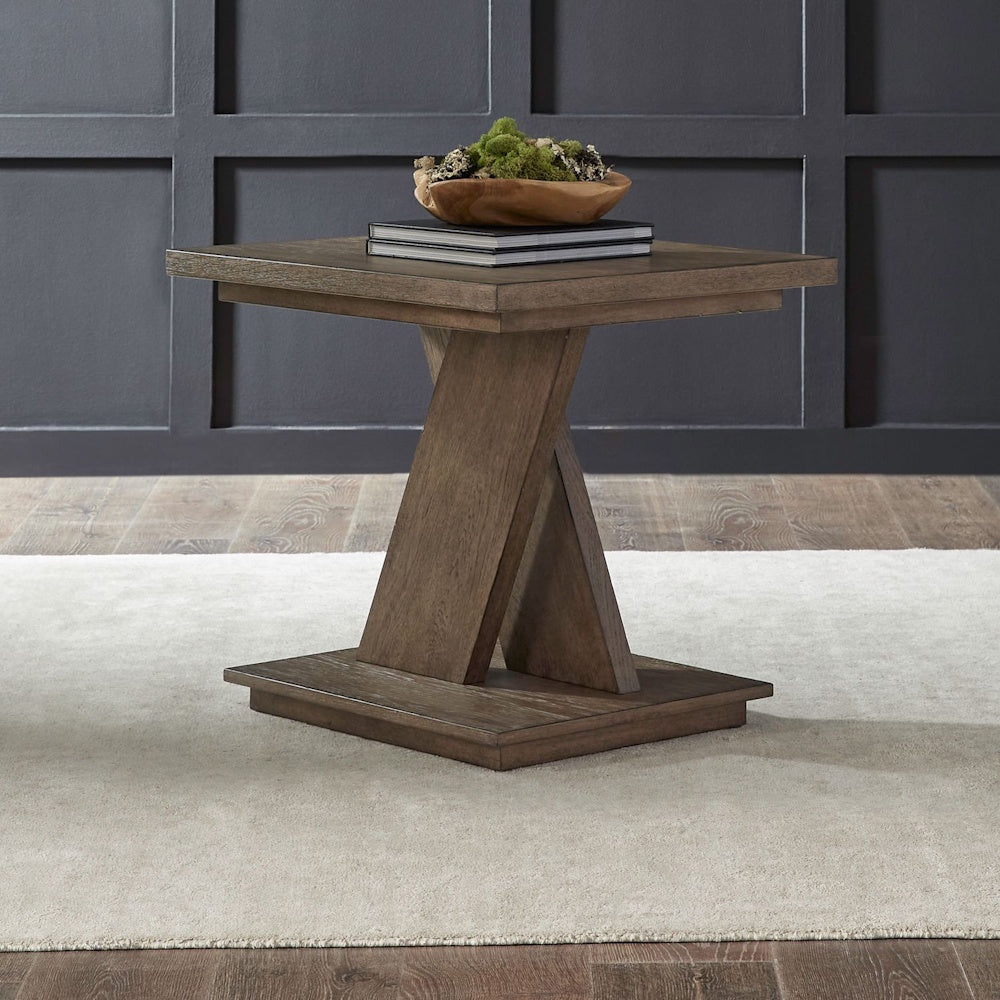 Modern square wood end table with an X-base design on a white rug against a dark paneled wall.