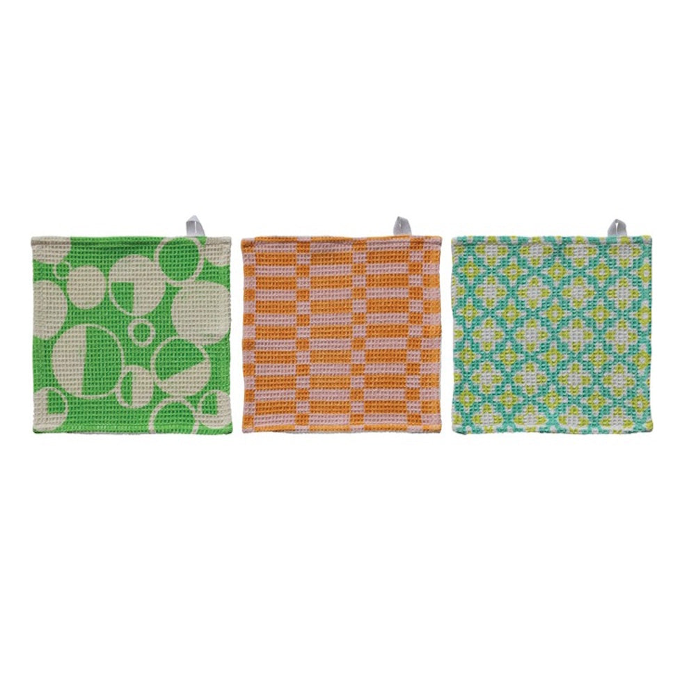 Three square waffle-weave dishcloths with green circle, orange rectangular, and teal geometric patterns.