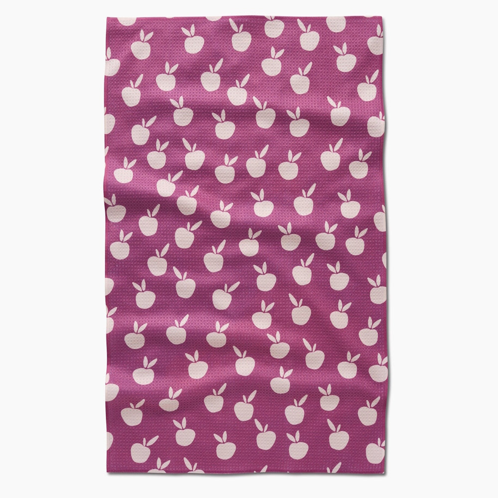 A rectangular, magenta waffle-weave tea towel covered in a repeating pattern of small, light pink apples.