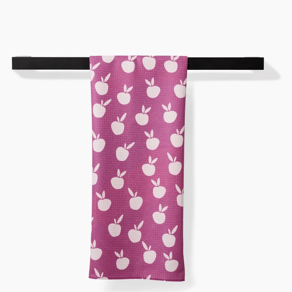 A purple tea towel featuring a white apple pattern hanging from a black bar.