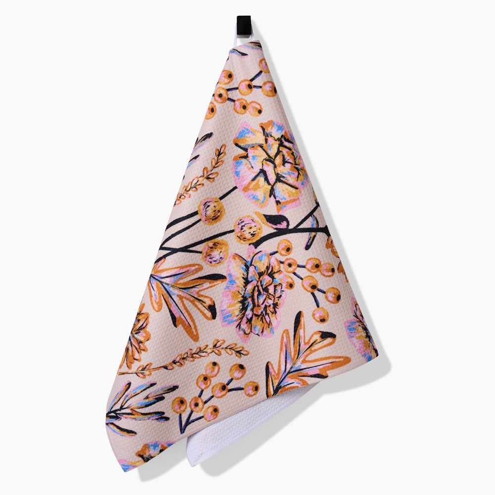 Hanging beige tea towel decorated with an illustrated autumn bouquet of yellow flowers and orange berries.
