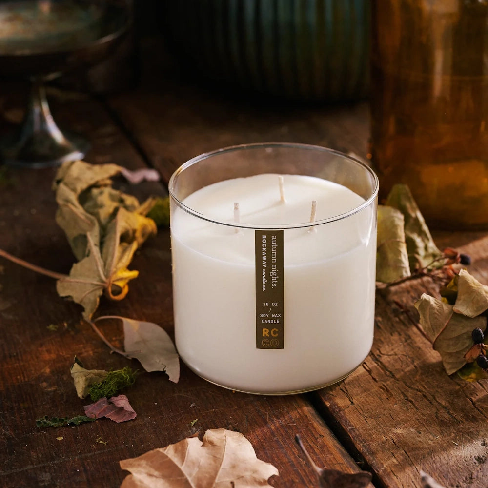 Rockaway Candle Co. Autumn Nights 16 oz soy wax 3-wick candle on a rustic wooden table with dried leaves.