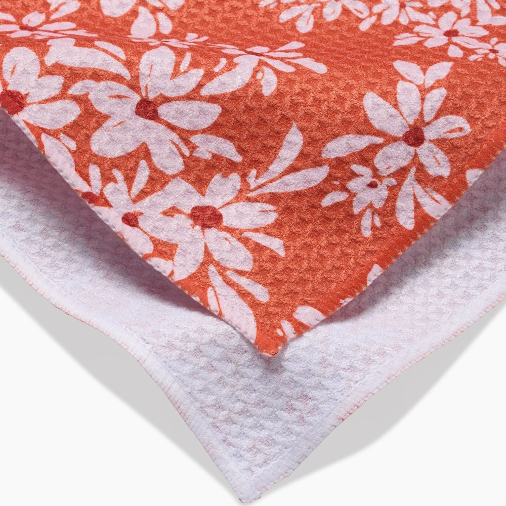 Close-up of a textured orange tea towel featuring a white floral pattern with a plain white underside.