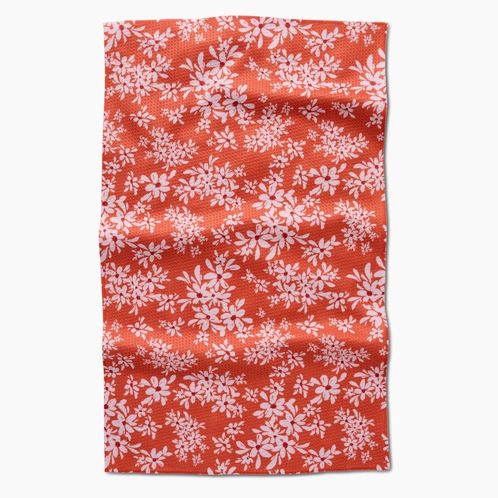Flat-lay view of an orange-red tea towel covered in a repeating pattern of small white and pink flowers.