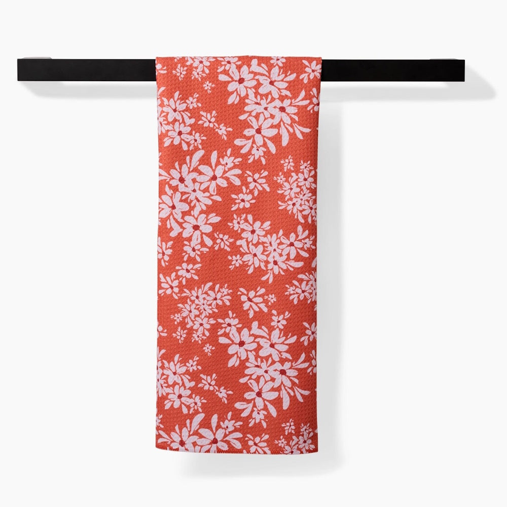 An orange kitchen towel with a white floral pattern hanging straight over a black modern towel bar.
