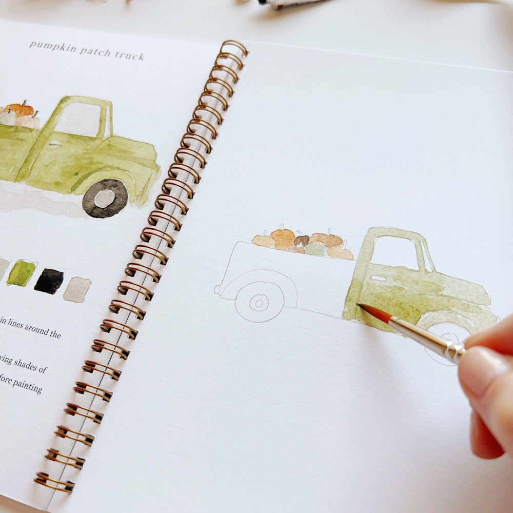 Close-up of a hand using a paintbrush to color a green vintage truck in an art workbook.