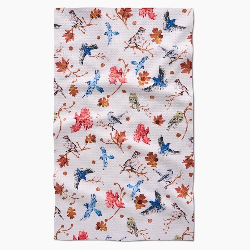 A tea towel with a repeating pattern of colorful birds and autumn leaves on delicate branches.