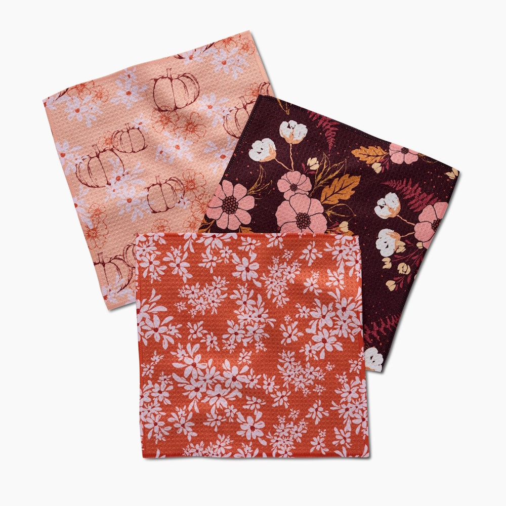 Three cloth napkins with autumn floral and pumpkin patterns in peach, burgundy, and burnt orange colors.