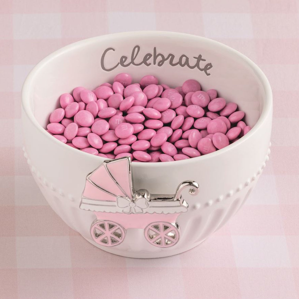 Pink candies in a white "Celebrate" baby shower bowl with a pink stroller charm on a checkered background.