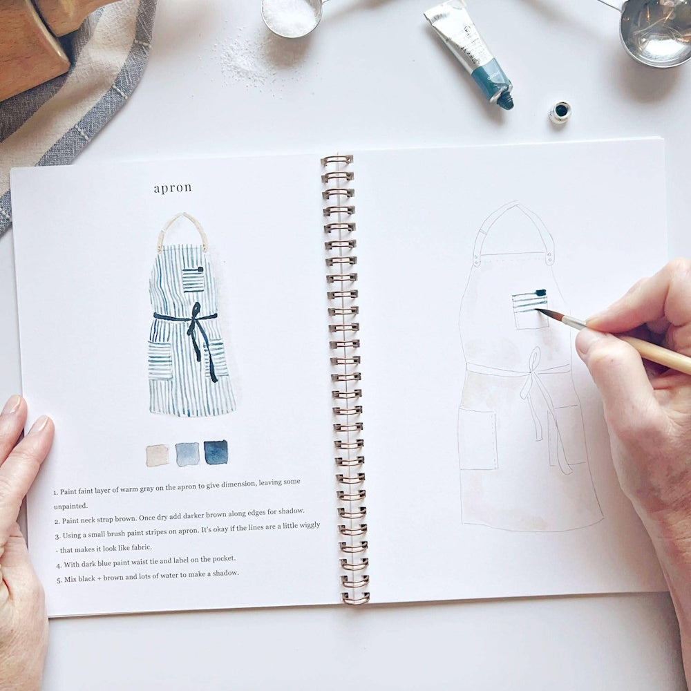Watercolor workbook page showing a blue striped apron illustration being painted with a brush on a white desk.