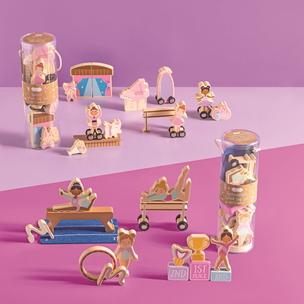 Wooden ballet and gymnastics toy sets with figures, balance beams, and accessories on a pink and purple background.
