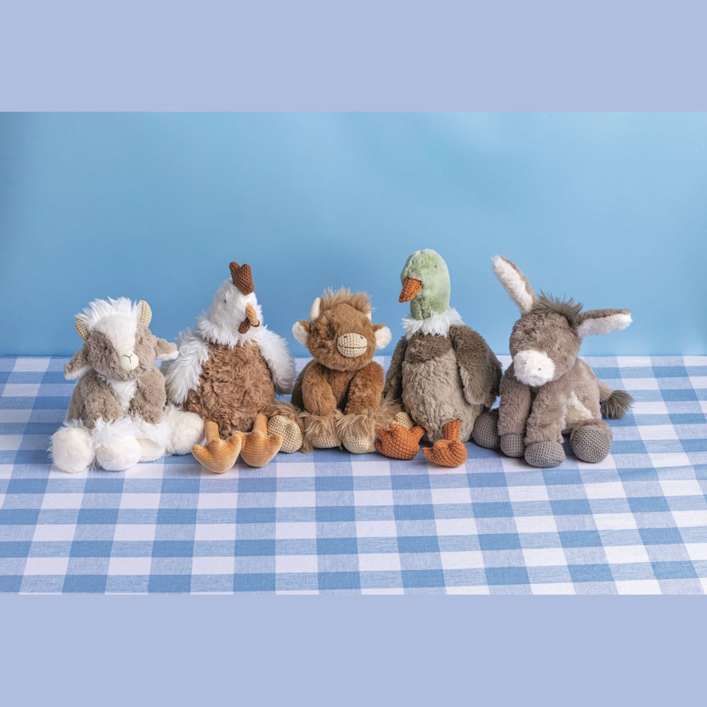 Five plush barnyard animal toys, goat, chicken, cow, duck, and donkey, sitting in a row on a blue checkered surface.
