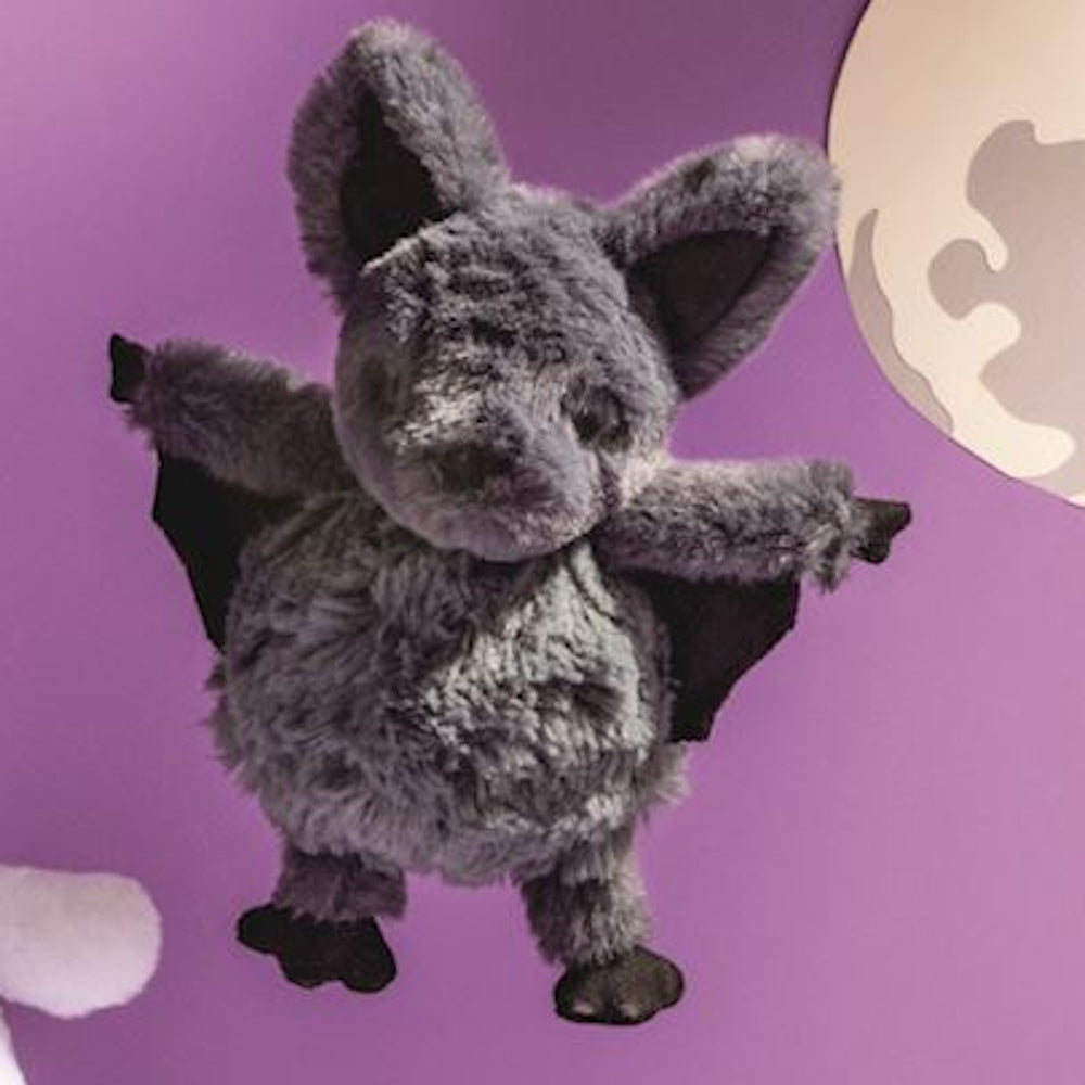 A fluffy grey plush bat with outstretched black wings, set against a purple background with a full moon.
