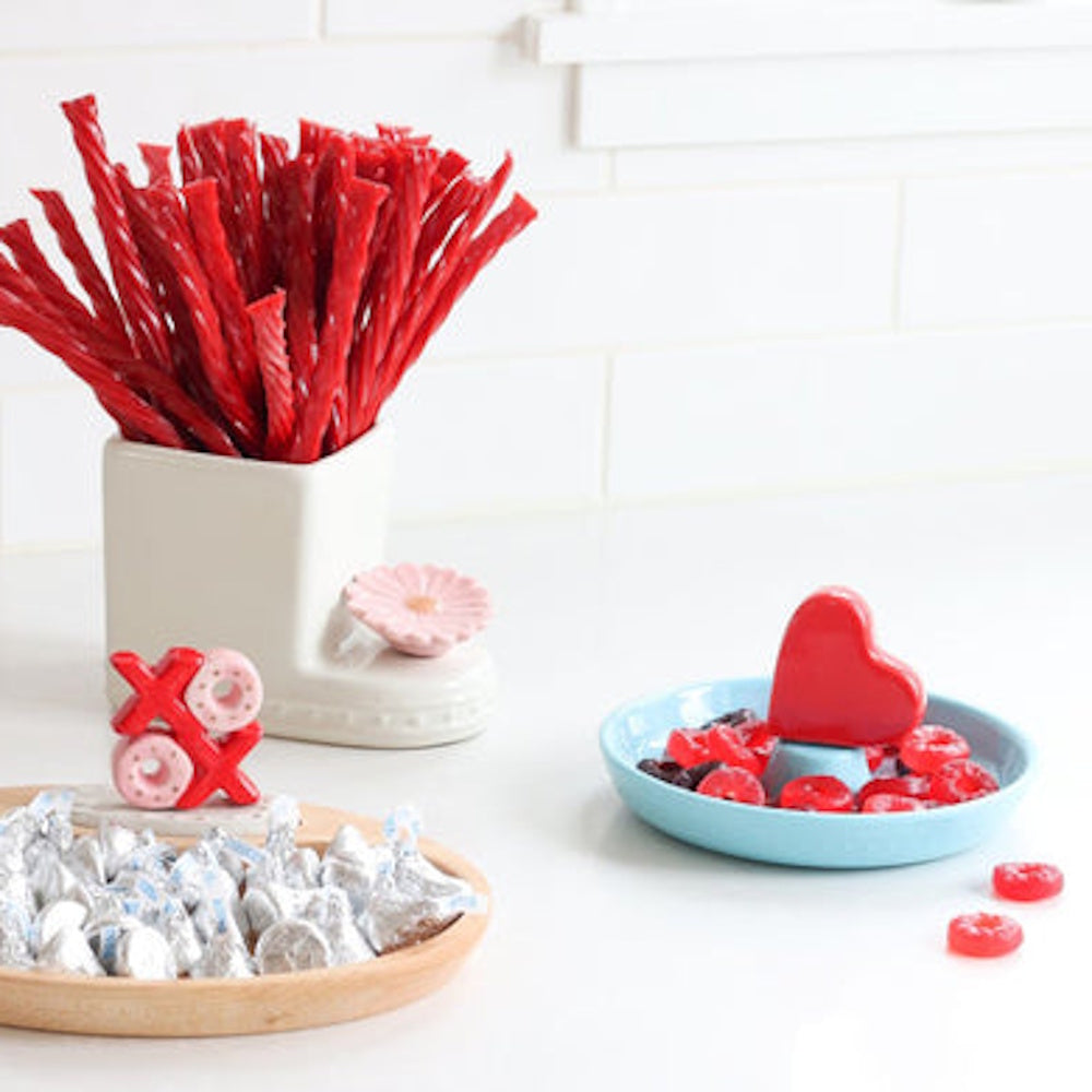 Red licorice, chocolate kisses, and Valentine candies arranged in decorative dishes on a white counter.