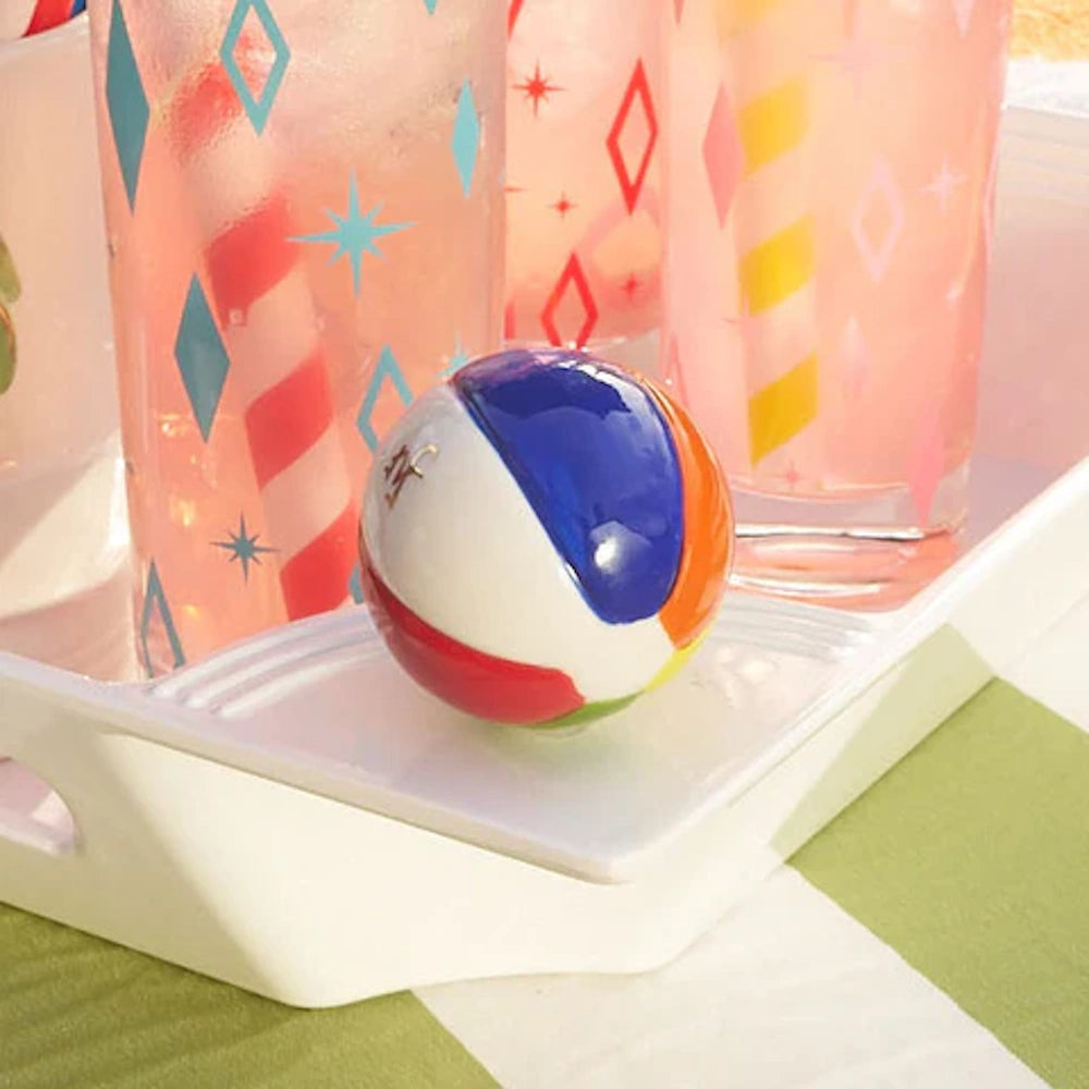 A colorful beach ball accessory on a white serving tray next to retro-printed glasses with pink drinks.