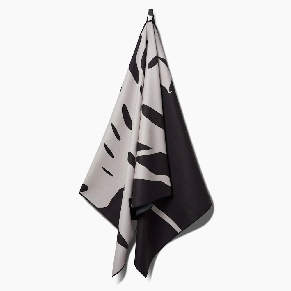 A black and white monstera leaf pattern towel hanging from a hook against a plain white background.