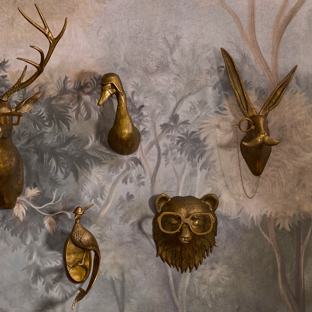 Brass animal head wall mounts, including a bear wearing glasses, displayed on a forest mural.