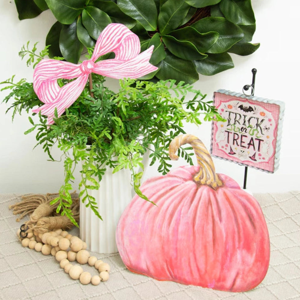 Pink pumpkin cutout with a matching striped bow in a green planter, Trick or Treat sign, and a leafy wreath.