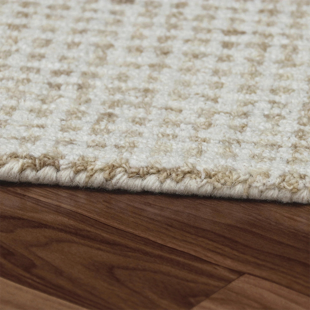 Close-up of a textured cream and beige patterned area rug on a dark wood floor.