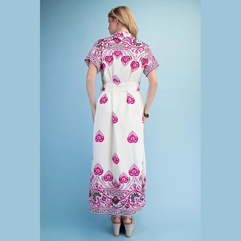 A woman in a white maxi shirt dress with fuchsia-colored floral patterns viewed from behind on a blue backdrop.