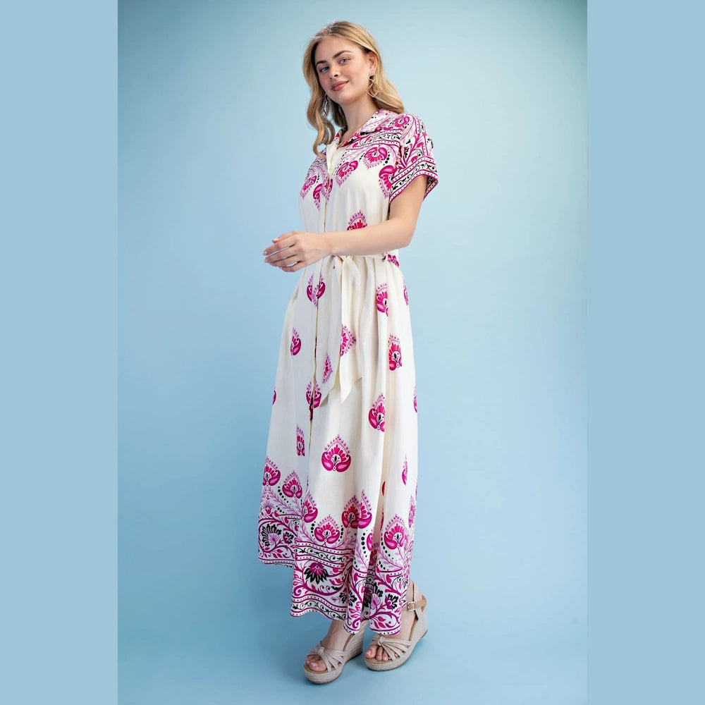 Woman in a berry-mix printed short-sleeve maxi shirt dress with a waist tie and wedge sandals against a blue backdrop.