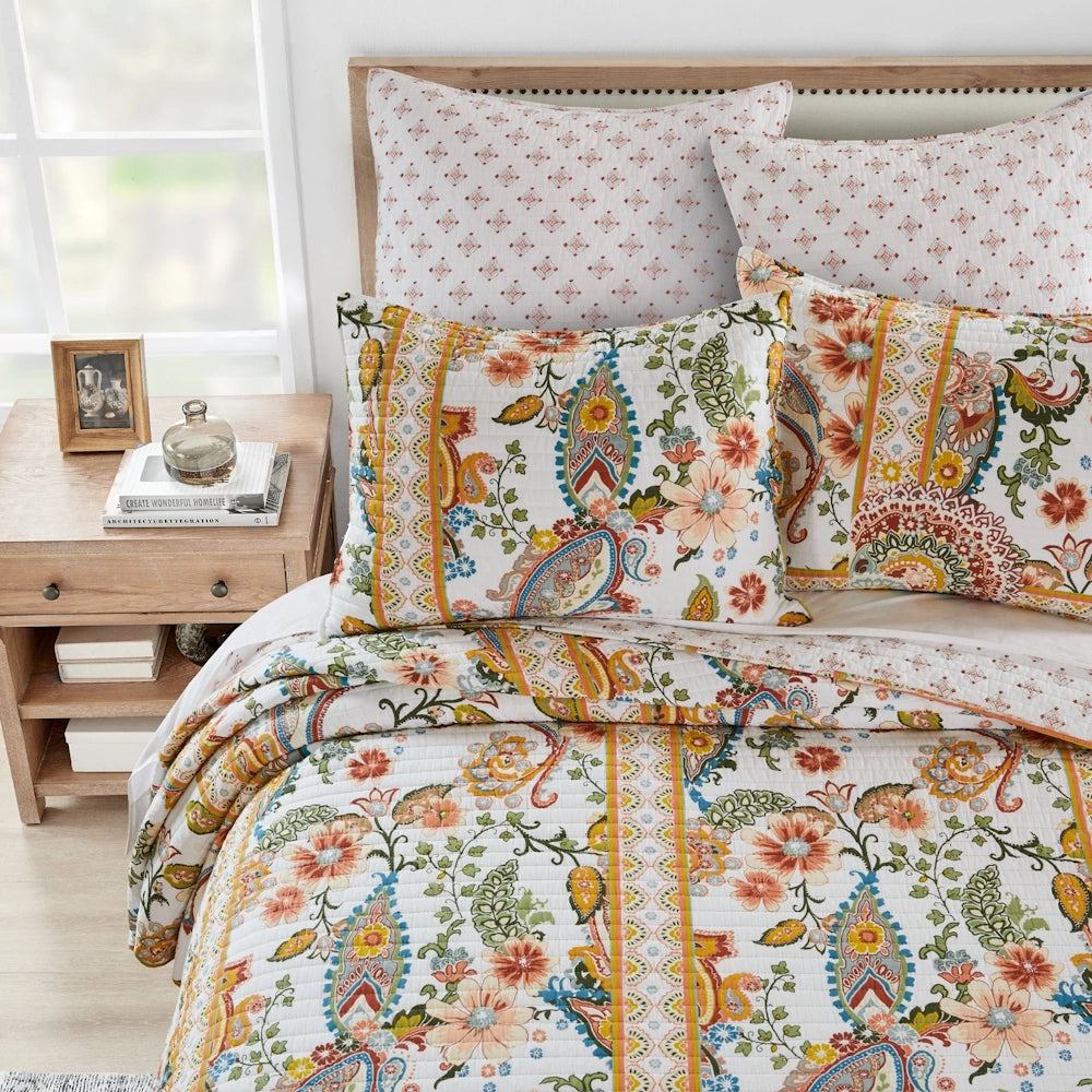 Top-down view of a bed styled with a colorful paisley quilt and matching pillow shams, with a wooden nightstand next to it.