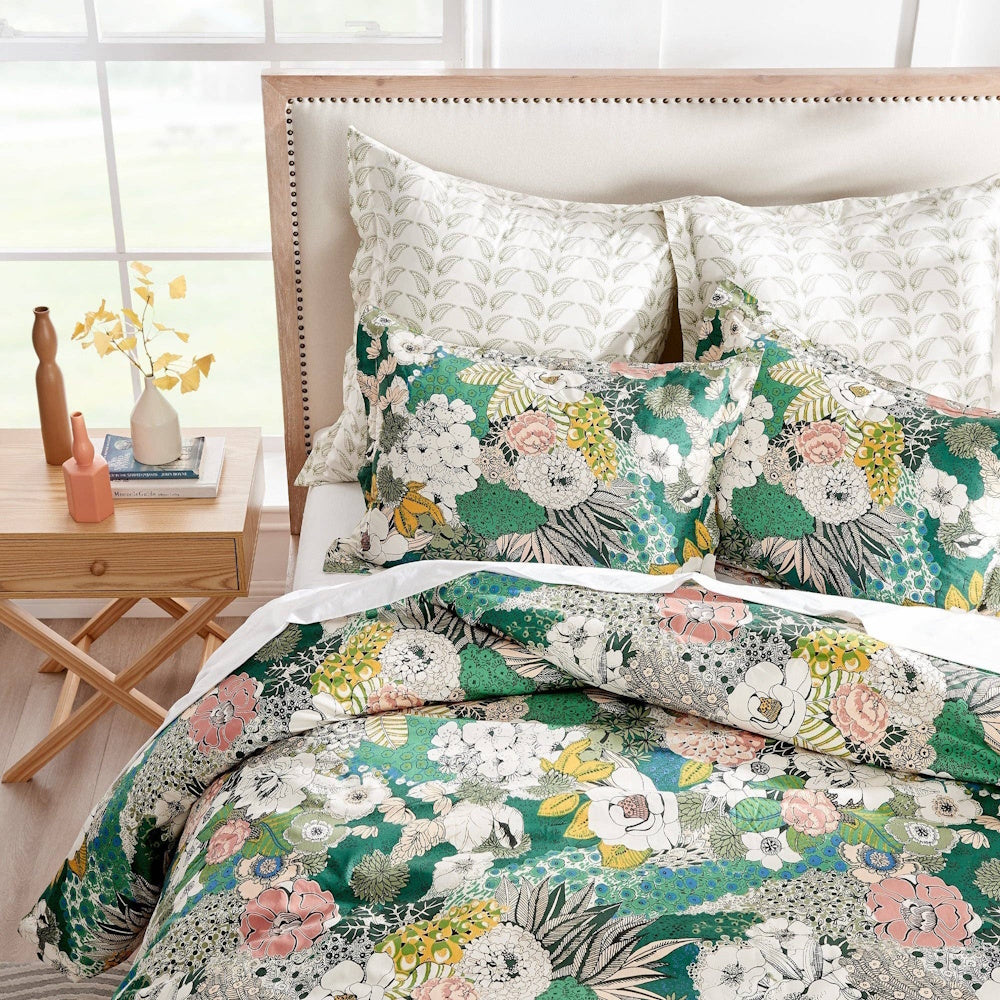 Bed dressed in vibrant floral green comforter and matching pillows against a neutral upholstered headboard.