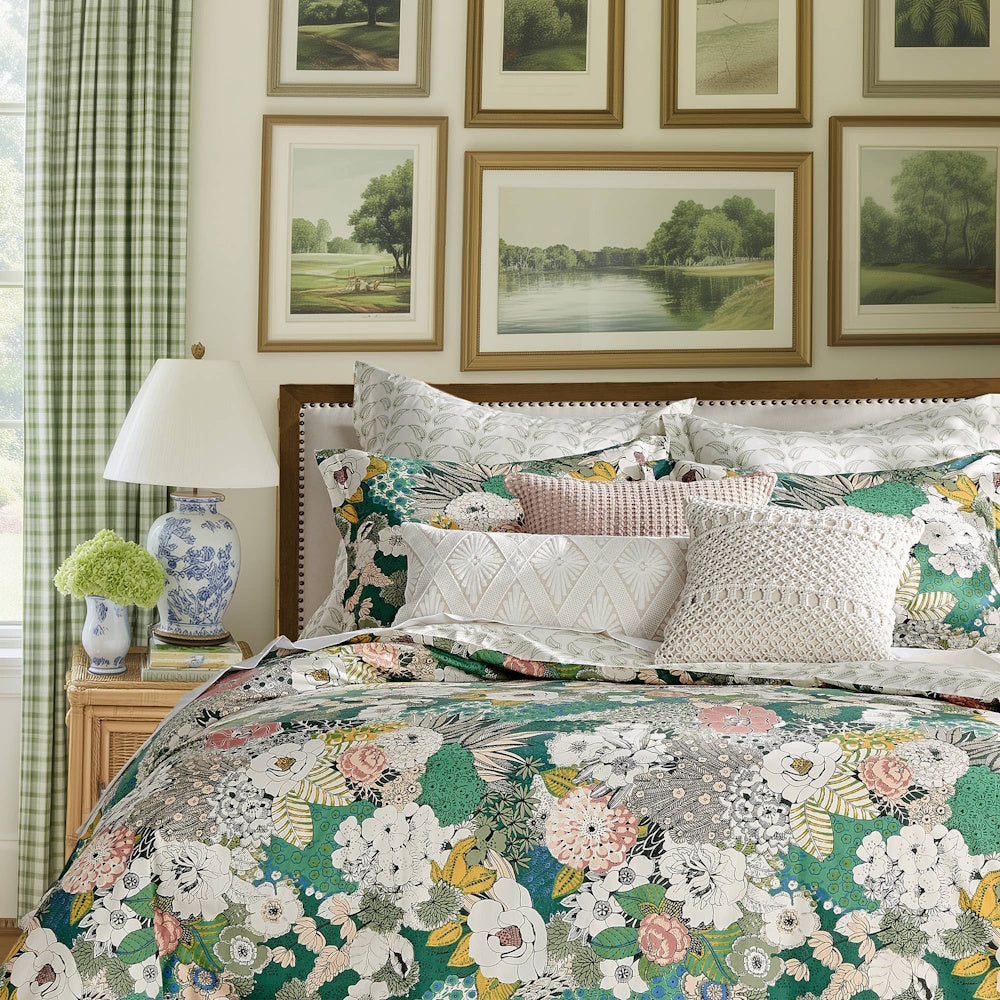 Bed styled with a green and pink floral comforter, matching shams, throw pillows, and framed landscape art.
