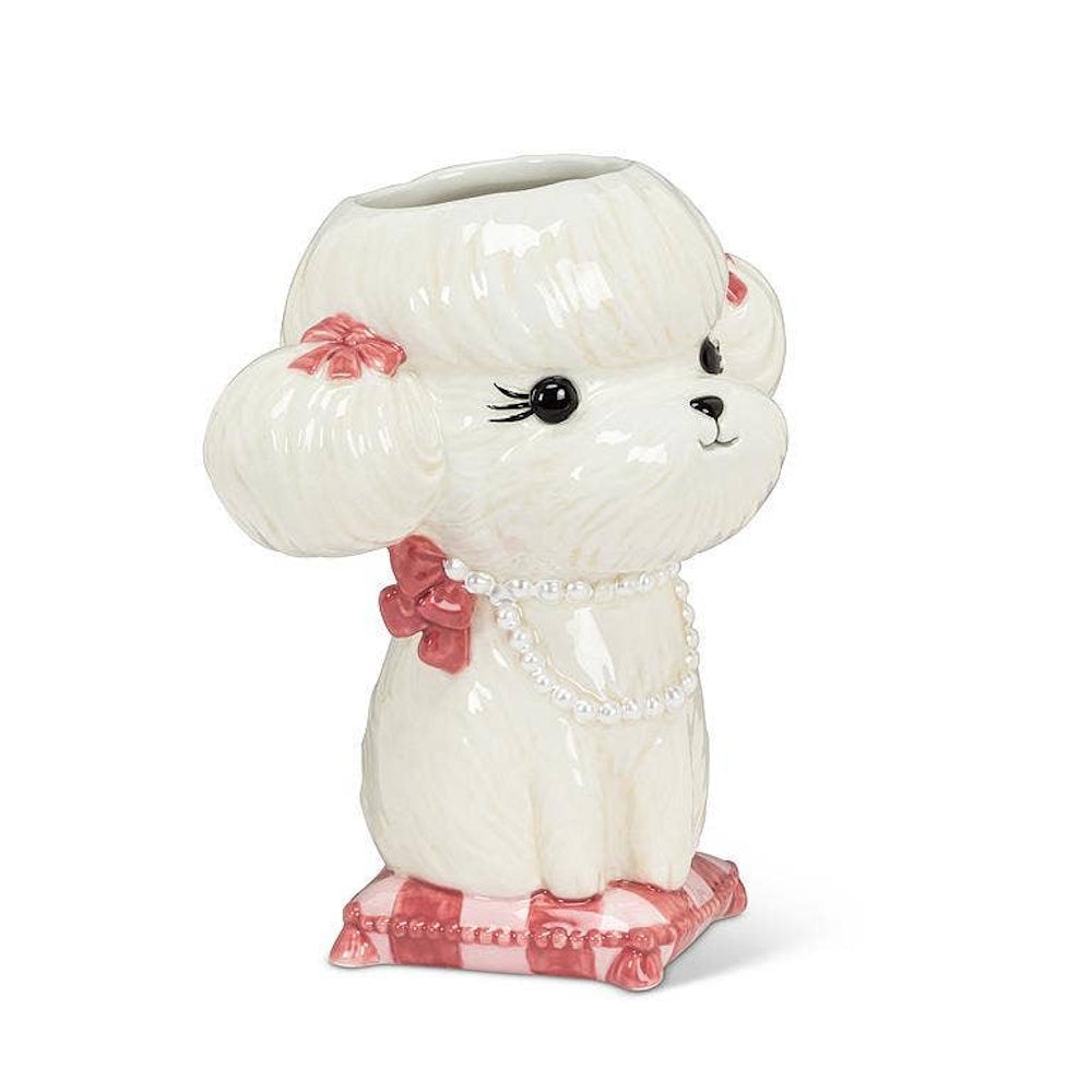 White ceramic poodle vase wearing a pearl necklace, sitting on a pink and white tufted cushion.